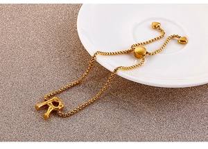 Detail of gold letter R pendant in bamboo style on adjustable heart clasp bracelet