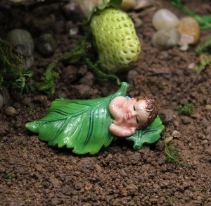 Detailed view of leaf-wrapped baby resin figurine in miniature garden landscape