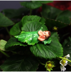 Macro shot of a sleeping baby fairy figurine nestled in green leaves for garden decor
