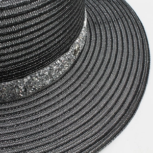 Detail of hollow straw hat with sparkling rhinestone band and round metal logo charm