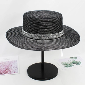 Detail of a black flat top straw hat with a sparkling silver sequin band on a stand