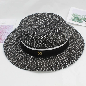 Close-up of woven boater hat with black ribbon and gold metal M hardware detail