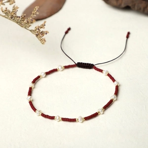 Close-up of handmade woven bracelet with red beads, freshwater pearls and adjustable cord