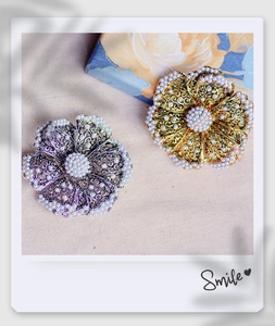 Macro detail of gold and silver flower brooches with white pearls on beige fabric background