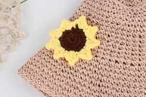 Detail of pink straw hat featuring a handcrafted crochet sunflower and woven texture
