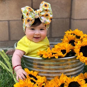 Detail of infant headband with large sunflower bow on baby model in outdoor setting