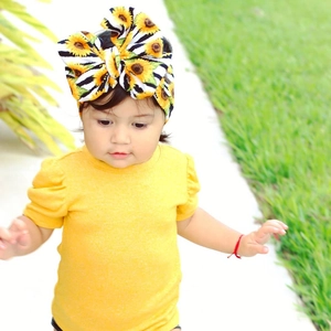 Baby girl wearing a yellow top and sunflower zebra print bow headband in outdoor setting