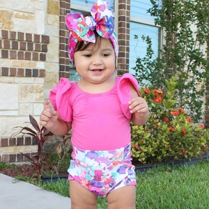 Detail of floral baby headband and ruffled pink cotton top worn by a smiling baby