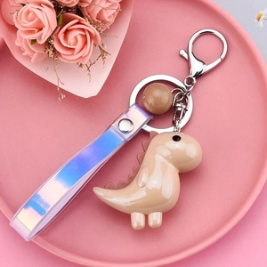 Detail of cute dinosaur keychain with holographic wrist strap and metallic clasp on a tray