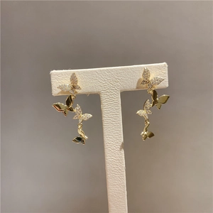 Detailed view of gold butterfly dangle earrings with crystals on a white T-stand display