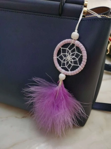 Close-up of pink dreamcatcher charm with purple feathers hanging on a handbag