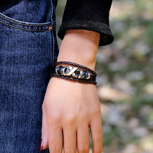 Close-up of multilayer leather bracelet featuring brass X-shaped metal charm and blue beads