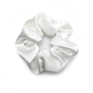 Close-up of white silk satin scrunchie showing soft fabric texture and pleated design
