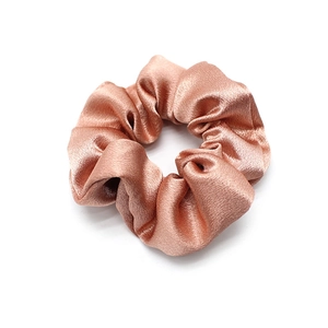 Detail of rose gold satin scrunchie with silky texture and elegant folds on white background
