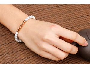 White marble bead and rose gold metal bead bracelet shown on a wrist over a bamboo mat