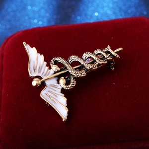 Vintage golden caduceus brooch with white enamel wings and snake details on velvet