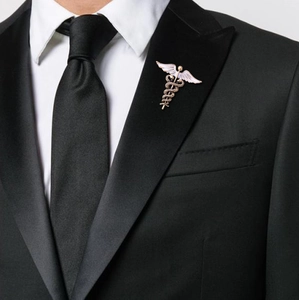 Close-up of golden Caduceus wing brooch with white enamel on a black suit lapel