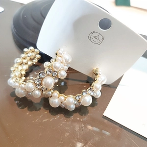 Macro detail of luxury C-shape hoop earrings with white pearls and sparkling rhinestones