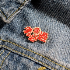 Detail of red enamel 'Pass Exam' goose brooch pinned on dark blue denim fabric texture