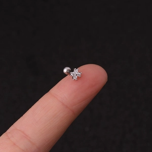 Macro shot of silver clover stud earring with zircons held on a fingertip for size
