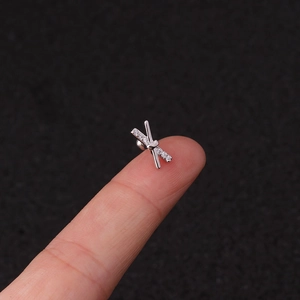 Close-up of a small silver cross stud earring with zircon inlay on a fingertip