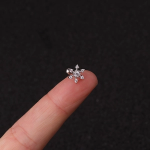 Macro shot of silver snowflake stud earring with clear zirconias on a fingertip