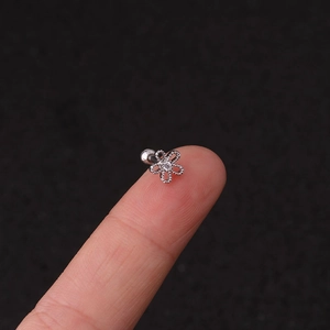 Detailed macro view of a silver flower stud earring with zircon on a fingertip