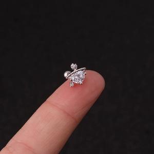 Macro shot of silver Saturn-shaped stud earring with clear gemstone on fingertip