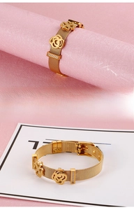 Gros plan sur un bracelet maille en acier doré avec breloques trèfle et fleurs coulissantes