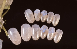 Detail of handcrafted cream white almond press-on nails with blue butterfly and glitter