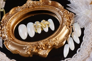Detail of opalescent white press-on nails with golden bow and sparkling rhinestones