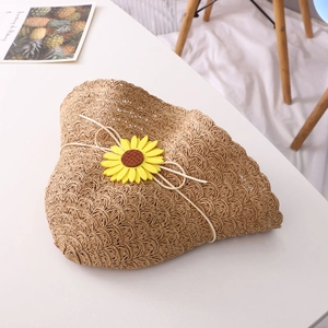 Straw sun hat with yellow sunflower decor on white table for beach sun protection