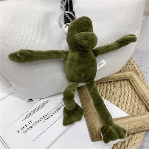 Detail of green plush frog keychain with KAWS-style X eyes on a white canvas bag