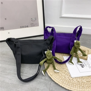 Detail of canvas crossbody bags in black and purple with cute plush frog pendant charms