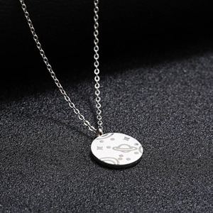 Collier médaille argentée avec planètes gravées et étoiles sur un fond noir texturé élégant