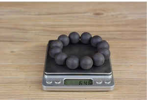 Deep brown ebony wood prayer beads being weighed on a digital scale showing 64.6g mass