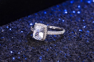 Detailed macro shot of a cushion-cut zircon halo ring on a sparkling blue glitter surface