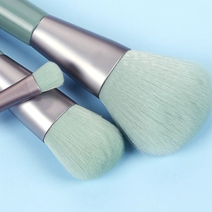 Detailed close-up of 3 mint green makeup brushes with silver ferrules on blue background