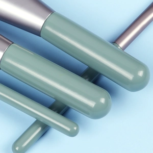 Macro detail of glossy sage green makeup brush handles with sleek metallic ferrule finish