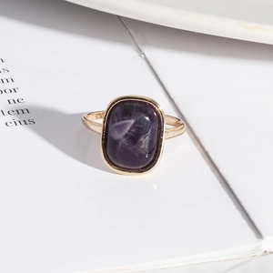 Detailed close-up of a gold-plated ring featuring a rectangular purple stone on a white book