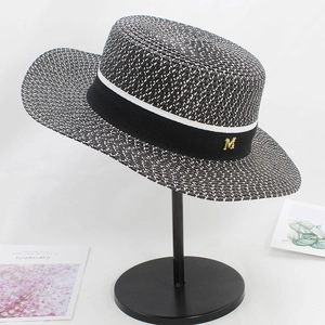 Detail of woven boater hat featuring black ribbon and golden metallic M ornament