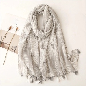 Écharpe aspect coton-lin avec imprimé floral gris et pompons sur fond clair apaisant
