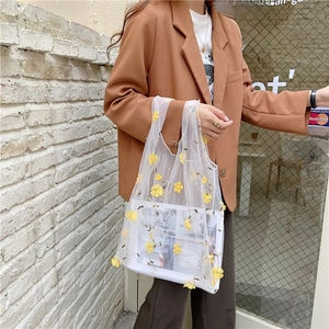 Detail of white mesh tote bag with delicate yellow flower embroidery in outdoor setting
