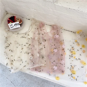 Detail of three embroidered tulle handbags in floral patterns on a white bench