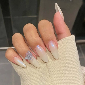 Detail of almond-shaped cream pearlescent press-on nails with silver 3D butterfly decor