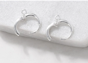 Detail of silver metallic hoop earring buckles with hanging loops on marble