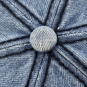 Dettaglio della corona del berretto in denim blu con cuciture e bottone superiore