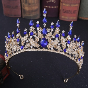 Close-up of Baroque gold crown with blue teardrop rhinestones and intricate floral patterns