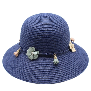 Detail of navy blue woven straw hat with delicate fabric flowers and gold tassel accents