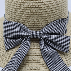 Detailed close-up of a straw sun hat featuring a large black and white gingham bow detail